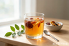A glass of warm herbal tea with red dates, goji berries and tangerine peel on a wooden table in morning light — a Sanfu summer wellness ritual